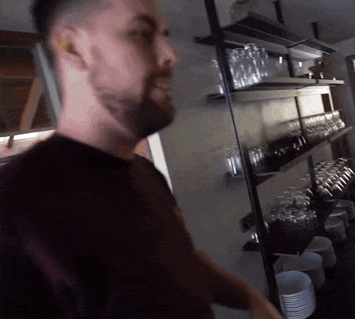 a man stands in front of a shelf full of glasses