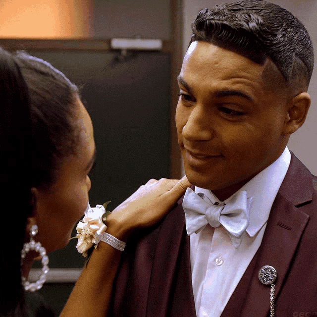 a man in a suit and bow tie is being touched by a woman wearing a flower bracelet