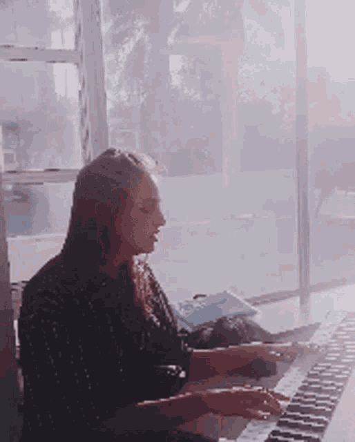 a woman is playing a keyboard in front of a window in a room .
