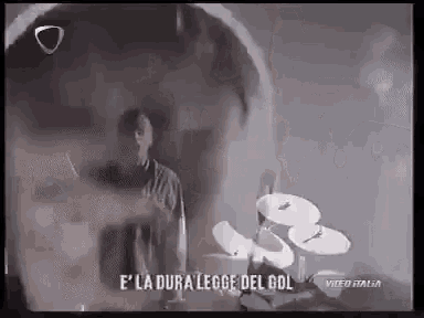 a man is standing in front of a drum set with the words e ' la dura legge del gol on the bottom .