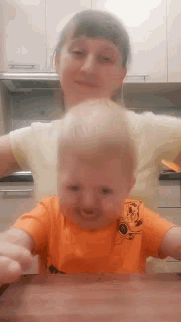 a woman is holding a baby in her arms who is wearing an orange shirt