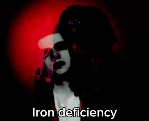 a woman with curly hair is standing in front of a purple wall with the words iron deficiency written on it .