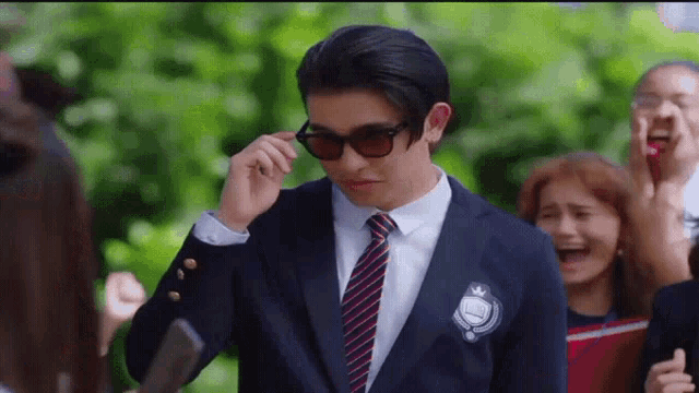 a man wearing a suit and tie is adjusting his sunglasses