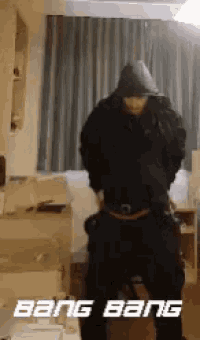 a man in a hooded jacket is dancing in a room with the words bang bang on the bottom .