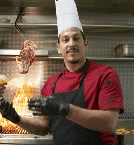 a chef is holding a piece of meat in front of a grill