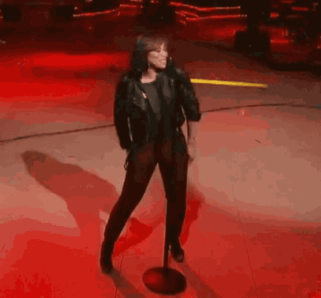 a woman is singing into a microphone on a stage in front of a red background .