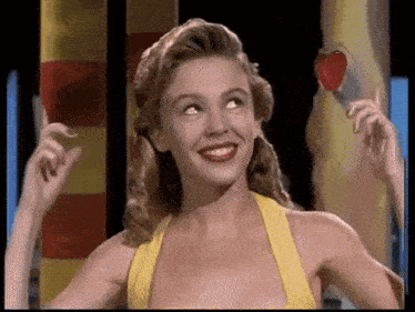 a woman in a yellow dress is smiling and holding a heart shaped lollipop