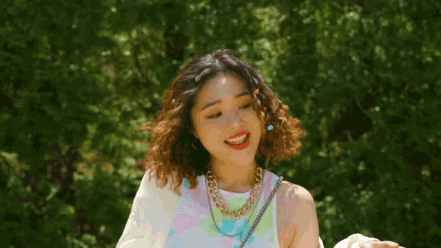 a woman wearing a necklace and earrings is standing in front of trees .