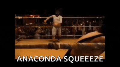 two men are wrestling in a ring with the words `` anaconda squeeze '' written above them .