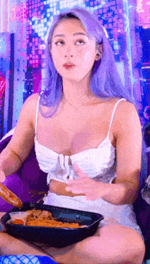 a woman with purple hair is sitting on a couch eating a meal