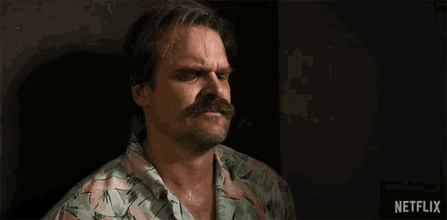 a man with a mustache is standing in front of a netflix logo