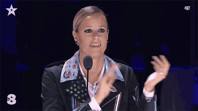 a woman is applauding in front of a microphone with the number 8 in the corner