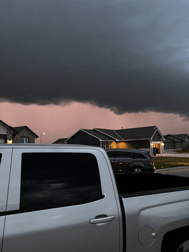 a white truck is parked in front of a house with a storm in the background