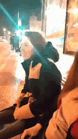 a woman in a black jacket sits next to another woman on a bench