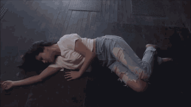 a woman in a white shirt and ripped jeans laying on the floor