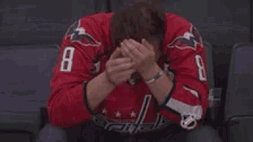 a man in a red jersey with the number 8 on it is sitting in a chair covering his face with his hands .