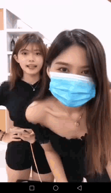 two women wearing masks are standing next to each other .