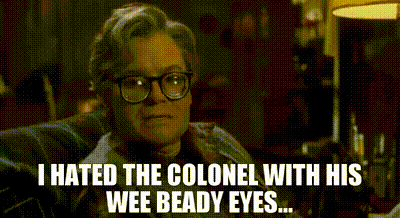 a man wearing glasses is sitting in a chair and says i hated the colonel with his wee beady eyes .