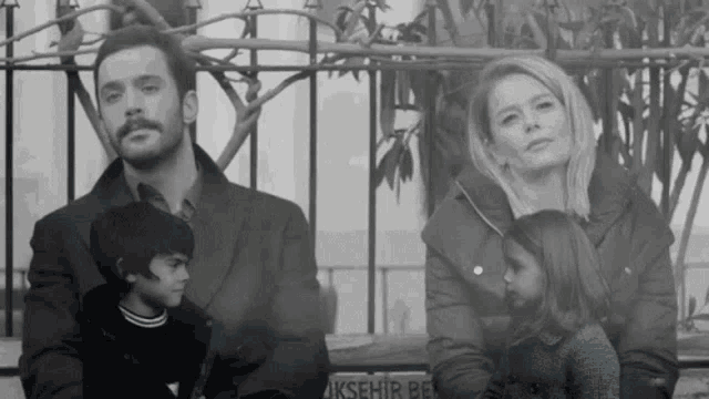 a black and white photo of a family sitting on a bench with a sign that says akşehir be