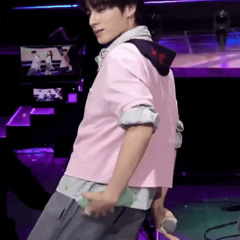 a man in a pink shirt and gray pants is standing on a stage holding a microphone .