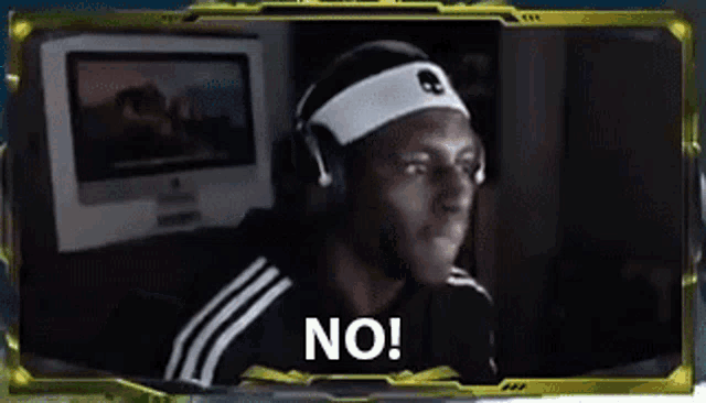 a man wearing headphones and a headband is sitting in front of a computer and says no .