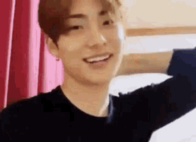 a young man is smiling and looking at the camera while sitting on a bed in a room .