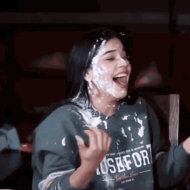 a woman wearing a green sweatshirt is covered in whipped cream .