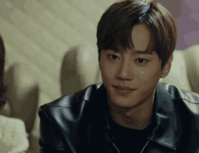 a young man wearing a black leather jacket and a black shirt is smiling