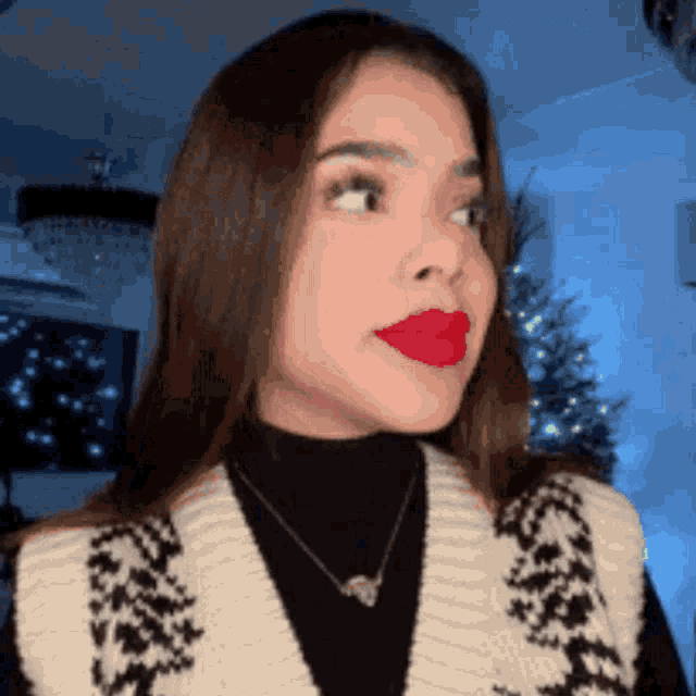 a woman with red lipstick on her lips is wearing a sweater vest and necklace .