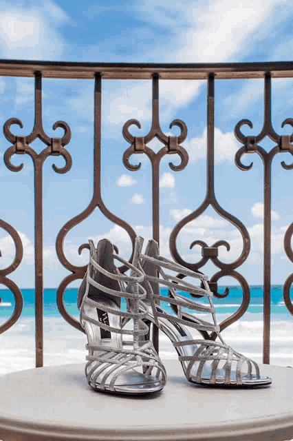 a pair of silver sandals sit on a table in front of a railing overlooking the ocean