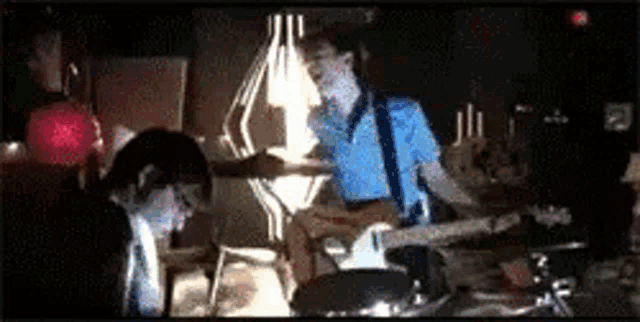a man in a blue shirt is playing a guitar in a dark room while a woman looks on .
