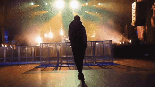 a silhouette of a person standing in front of a stage with a few lights on