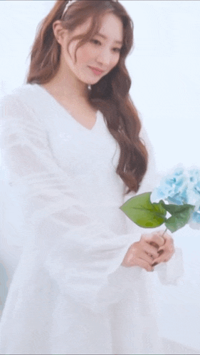 a woman in a white dress is holding a bouquet of blue flowers .