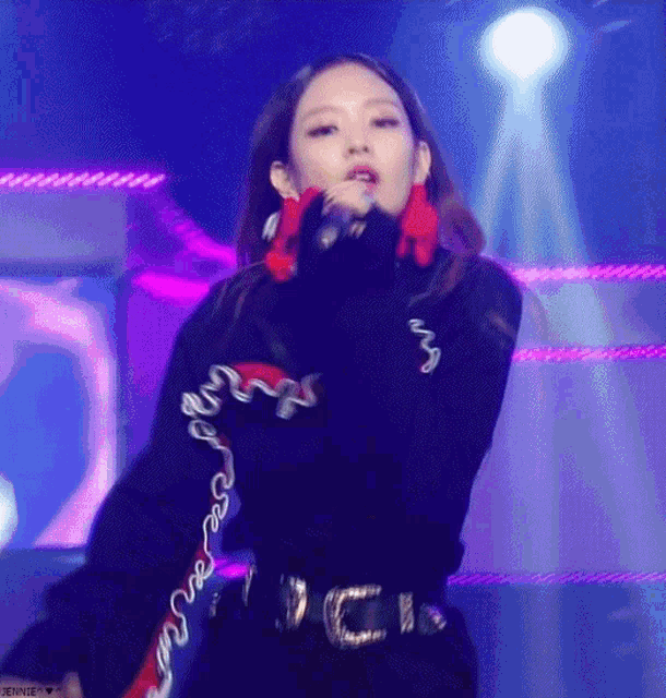 a woman is singing into a microphone while wearing a black sweater and red earrings .