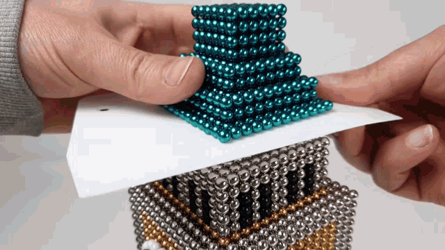 a person is holding a piece of paper with a stack of beads on top of it