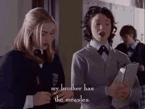 two girls in school uniforms are standing next to each other in a locker room and talking .