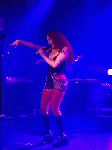 a woman singing into a microphone on a stage in front of a keyboard