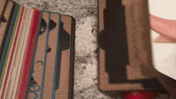 a person is holding a cardboard box next to a stack of books .