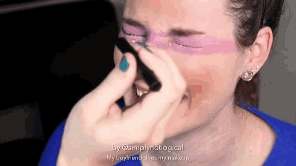 a woman wearing a blue shirt is applying makeup to her face