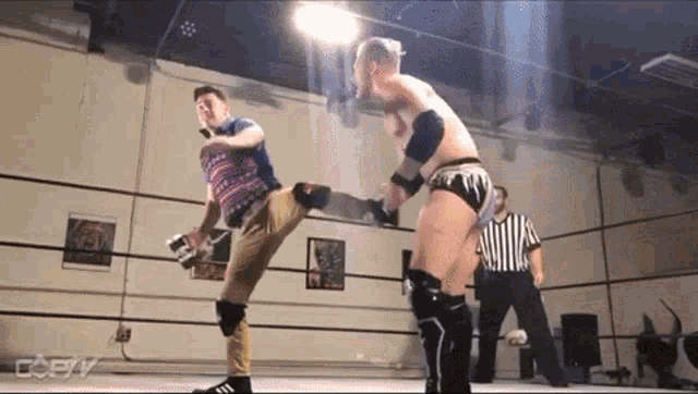 two men are wrestling in a ring and one of them is kicking the other .