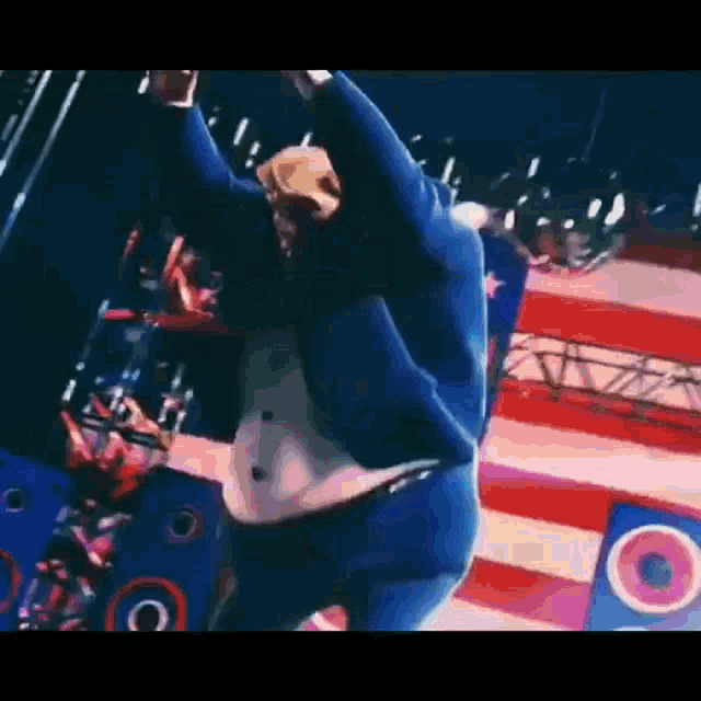 a man in a blue suit is dancing on a stage with an american flag in the background