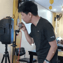 a man in a black shirt is singing into a microphone while standing in front of a speaker