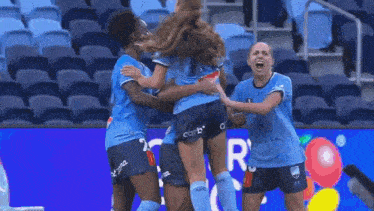 a group of female soccer players are hugging each other in front of a sign that says the lot off .