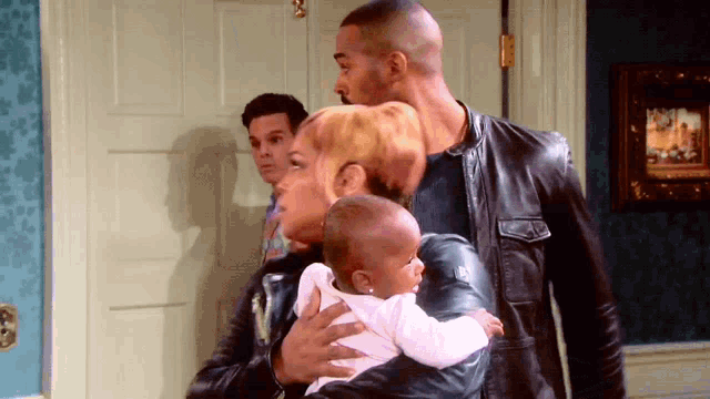 a woman is holding a baby in her arms while a man stands behind her