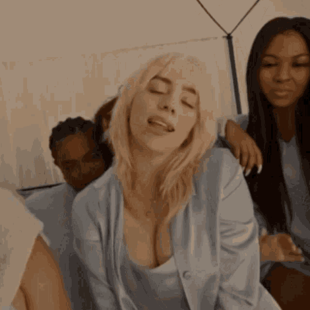 billie eilish is sitting on a bed with her eyes closed and her tongue sticking out