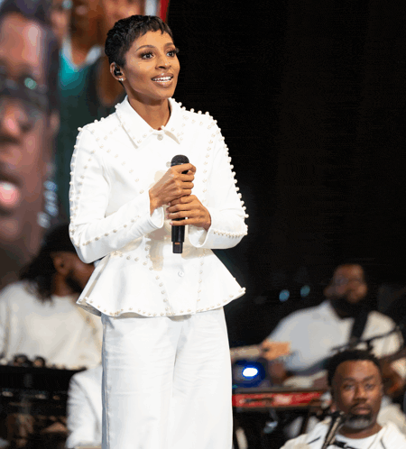 a woman singing into a microphone while wearing a white jacket