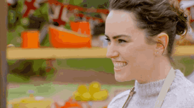 a woman wearing a sweater and apron smiles while standing in front of a table
