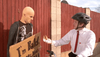 a man holding a sign that says " i 'm bald " talks to another man