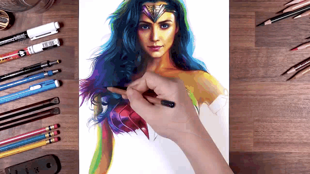 a person is drawing wonder woman with a pencil on a wooden table