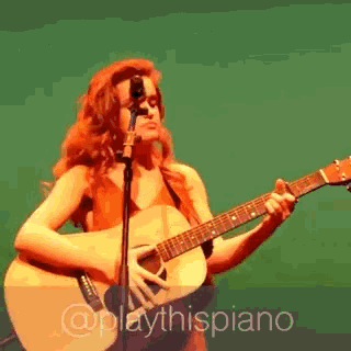 a woman singing into a microphone while holding a guitar in front of a green background